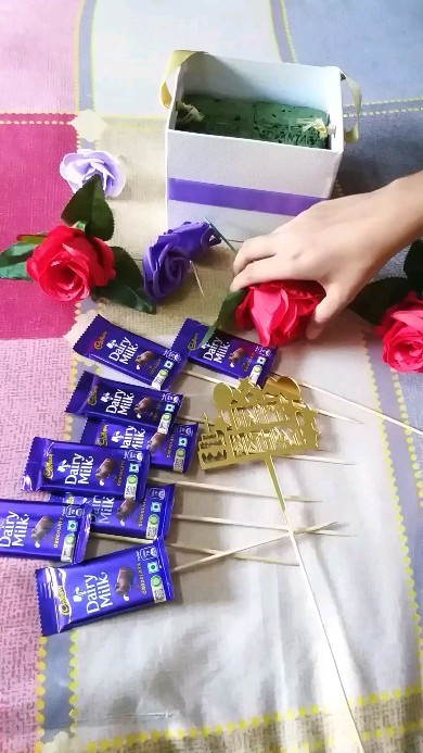 Hands arranging chocolate bars and paper flowers for a gift hamper