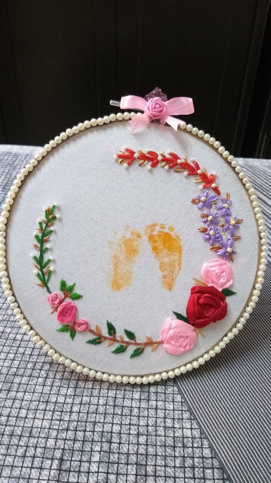 Floral embroidered hoop with a small pair of golden footprints in the centre